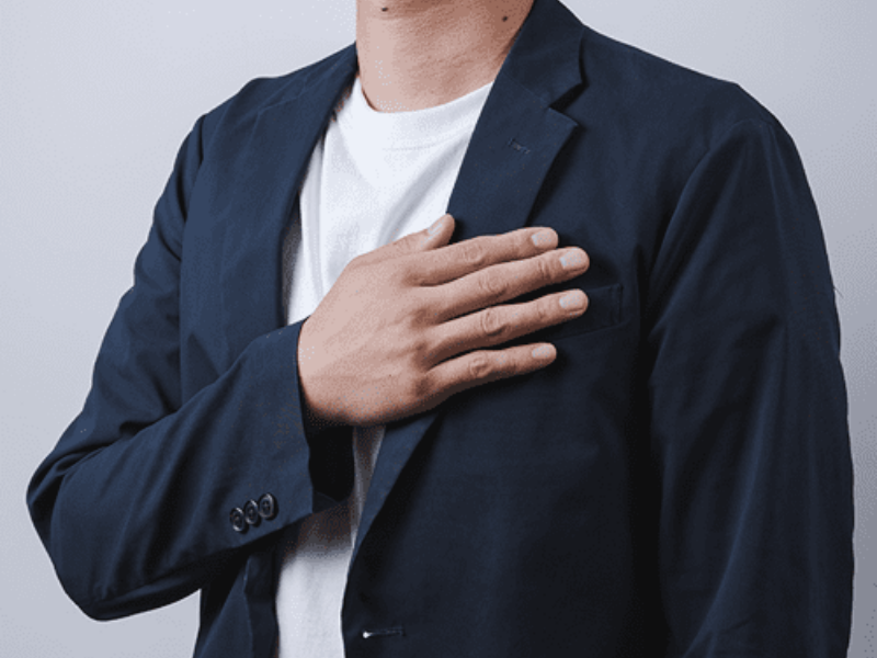 胸に手を当てるスーツ姿の男性の上半身。