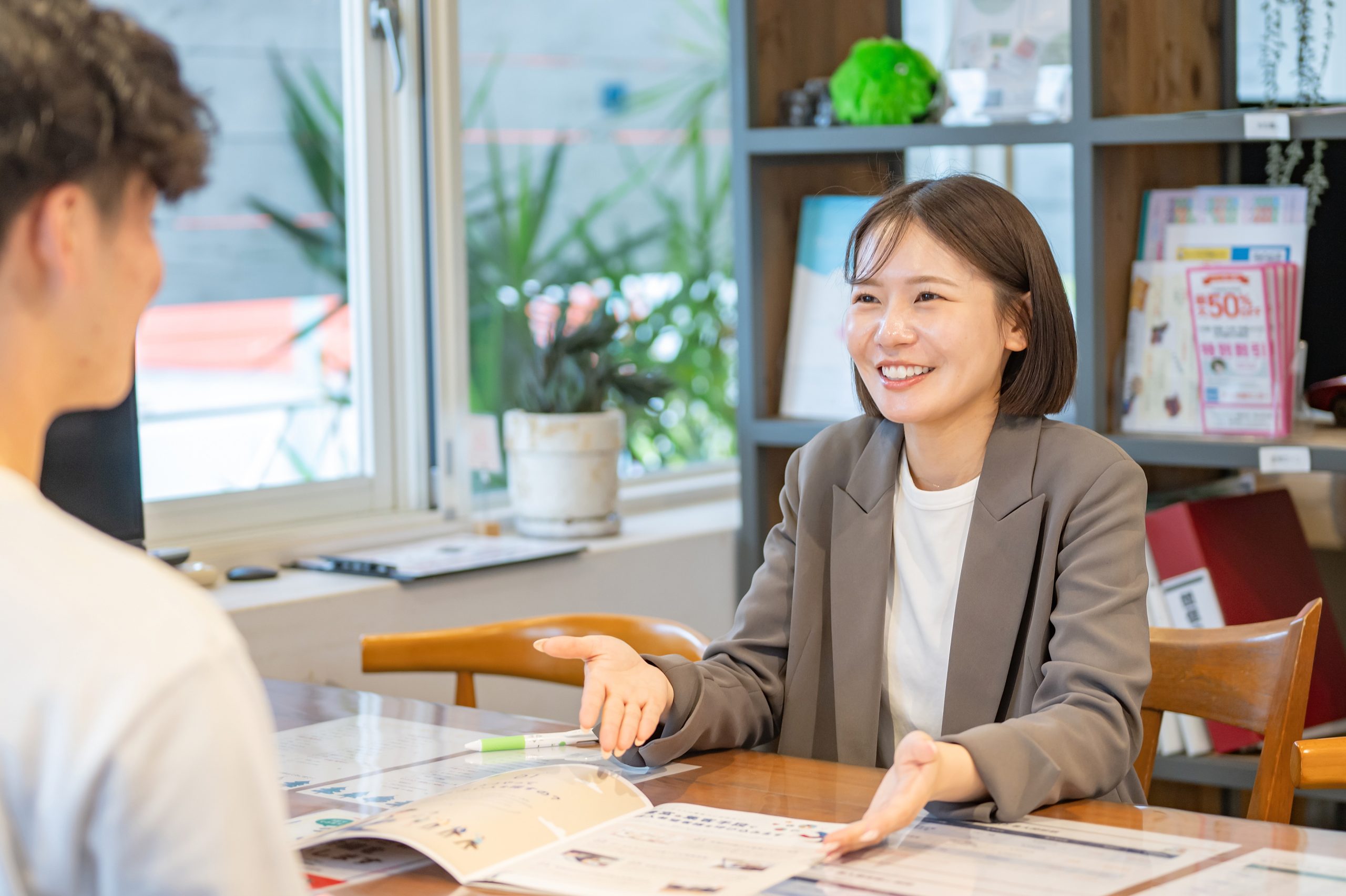 笑顔で説明する女性スタッフと向かい合って話を聞いている男性。テーブルには資料と電卓が置かれている。